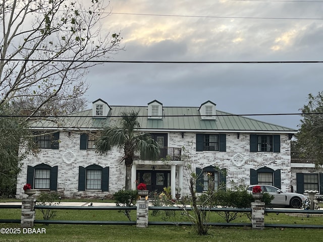 view of front facade featuring a balcony, a standing seam roof, a fenced front yard, and metal roof