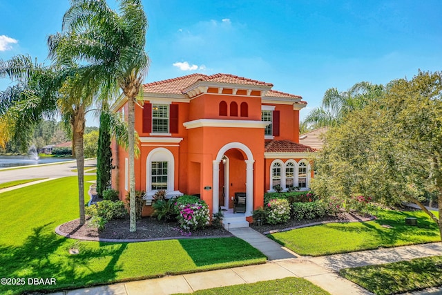 mediterranean / spanish-style home with a front yard, a tiled roof, and stucco siding