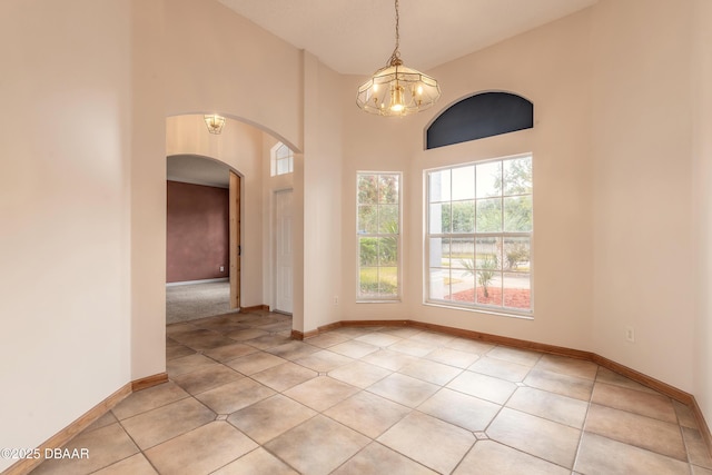 tiled spare room featuring a high ceiling and a chandelier