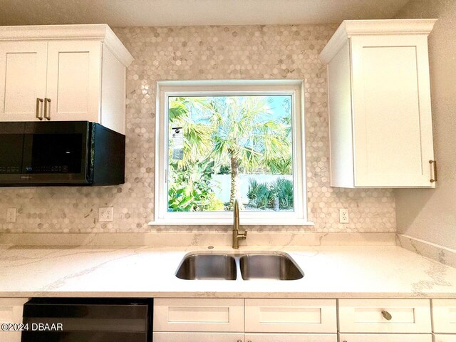 kitchen with light stone countertops, white cabinetry, sink, and dishwashing machine