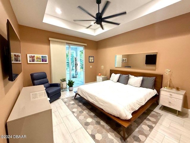 bedroom with ceiling fan, access to exterior, and a tray ceiling