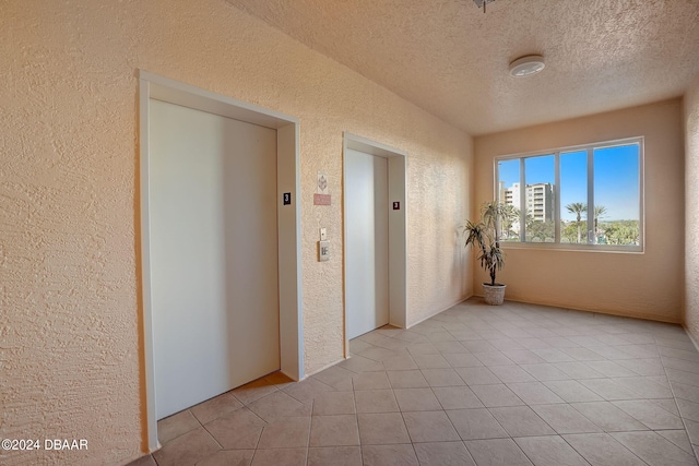 tiled empty room featuring elevator and a textured ceiling