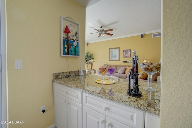 kitchen featuring ornamental molding, a textured ceiling, light stone countertops, white cabinets, and ceiling fan