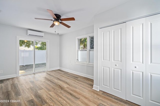 unfurnished bedroom featuring multiple windows, wood finished floors, baseboards, and a wall mounted air conditioner