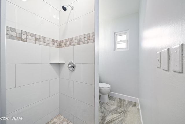 bathroom featuring toilet, tiled shower, and baseboards