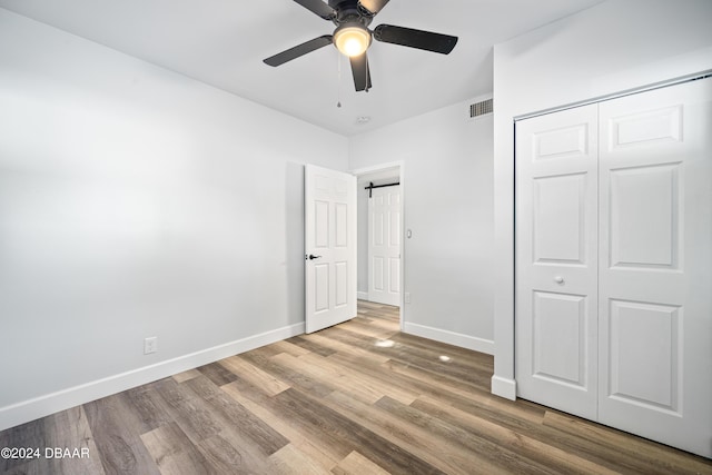 unfurnished bedroom featuring a barn door, wood finished floors, visible vents, and baseboards