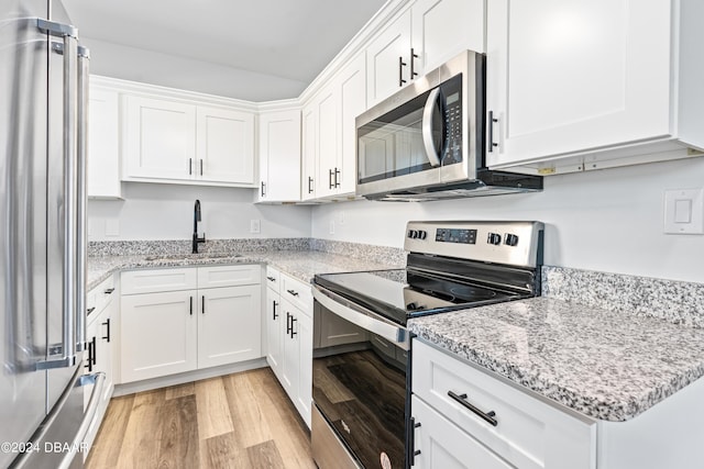 kitchen featuring a sink, light stone counters, white cabinetry, light wood-style floors, and appliances with stainless steel finishes