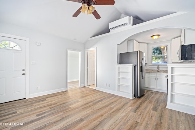 unfurnished living room with baseboards, light wood-type flooring, a wall unit AC, and vaulted ceiling