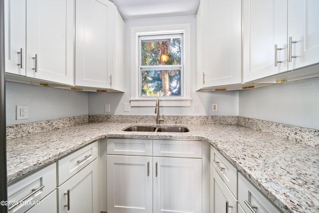 kitchen featuring a sink, light stone counters, and white cabinets