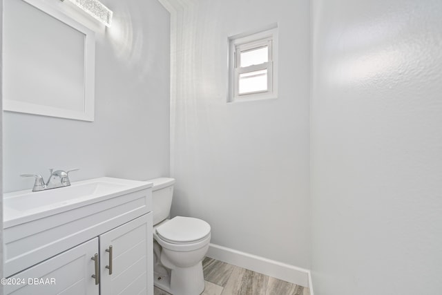 half bath featuring toilet, vanity, baseboards, and wood finished floors