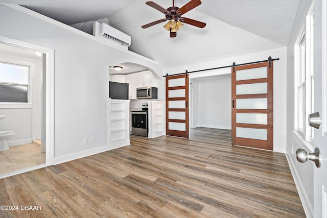 unfurnished living room featuring a wall mounted air conditioner, wood finished floors, a barn door, ceiling fan, and vaulted ceiling