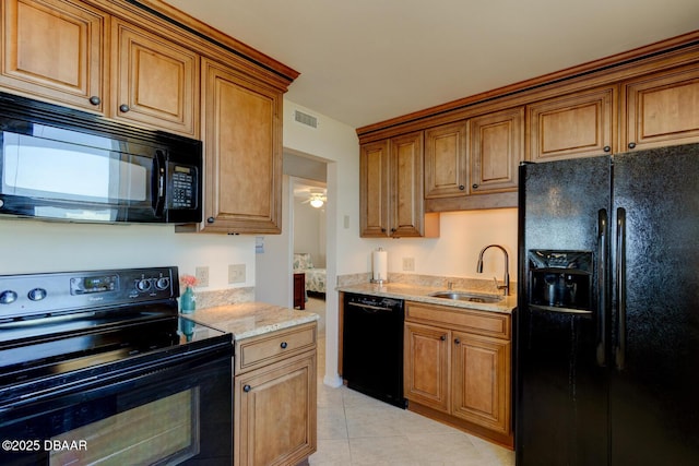 kitchen with light stone countertops, sink, light tile patterned floors, and black appliances