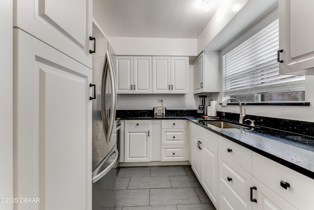 kitchen featuring sink, white cabinets, stainless steel refrigerator, and dark stone counters