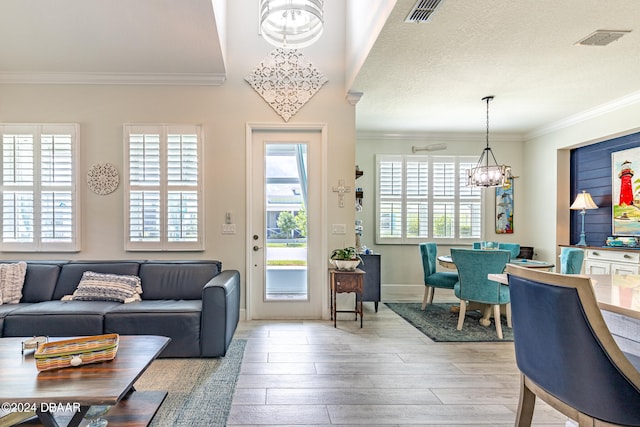 living room featuring light hardwood / wood-style floors, a textured ceiling, crown molding, and a notable chandelier