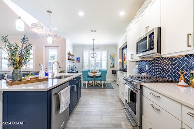 kitchen with white cabinetry, stainless steel appliances, hanging light fixtures, and sink