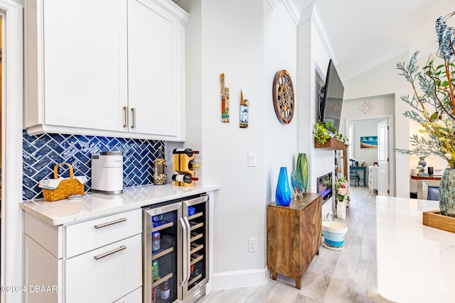 bar featuring beverage cooler, vaulted ceiling, white cabinets, light stone countertops, and light hardwood / wood-style flooring