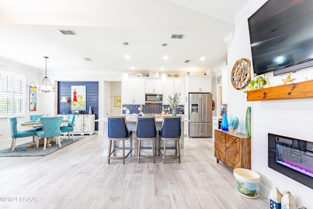 kitchen featuring white cabinetry, appliances with stainless steel finishes, pendant lighting, light hardwood / wood-style floors, and a kitchen breakfast bar