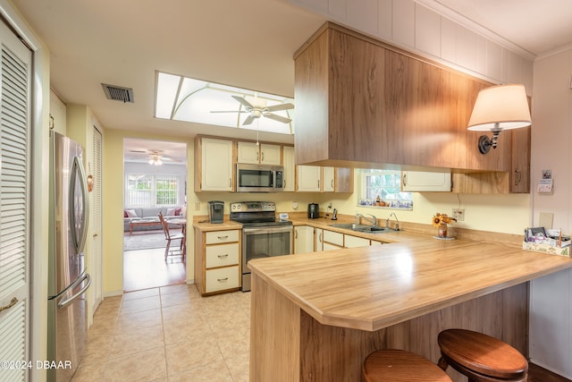 kitchen with sink, light tile patterned floors, ornamental molding, appliances with stainless steel finishes, and kitchen peninsula