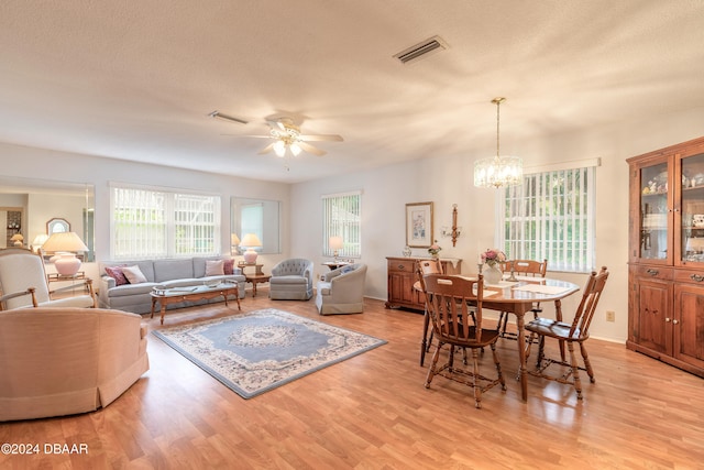 living room with ceiling fan with notable chandelier, light hardwood / wood-style floors, and a textured ceiling