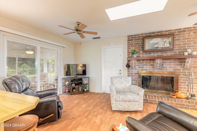 living room featuring a skylight, ceiling fan, wood-type flooring, and a brick fireplace