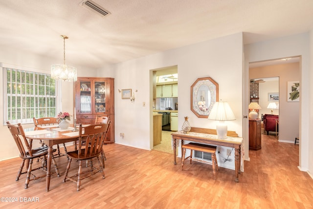 dining area with light hardwood / wood-style floors, a textured ceiling, and a notable chandelier