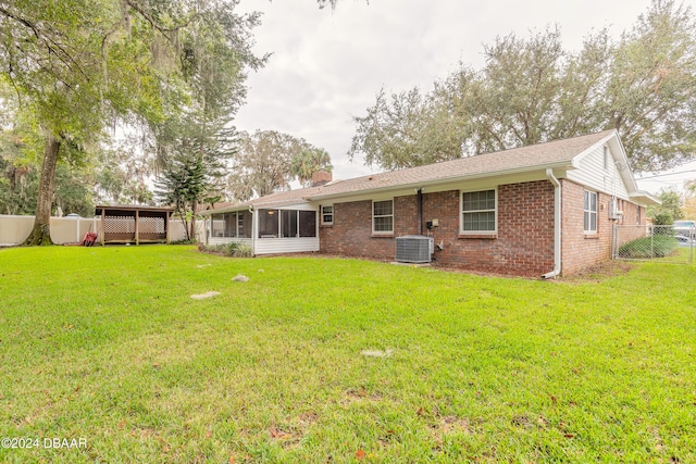 back of house with a sunroom, a storage unit, a lawn, and central AC