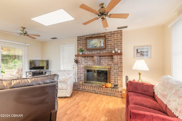 living room with a fireplace, wood-type flooring, a skylight, and ceiling fan