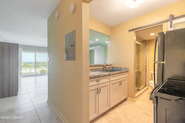 kitchen with a barn door, light tile patterned floors, fridge, light stone countertops, and sink