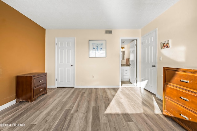 bedroom with connected bathroom, a textured ceiling, and light hardwood / wood-style flooring