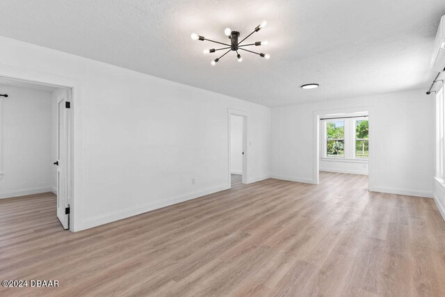 unfurnished room with a textured ceiling, light hardwood / wood-style flooring, and a notable chandelier