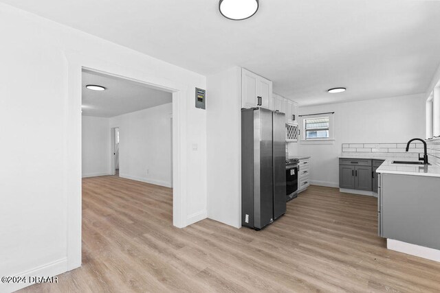 kitchen with light hardwood / wood-style floors, stainless steel appliances, white cabinets, decorative backsplash, and sink