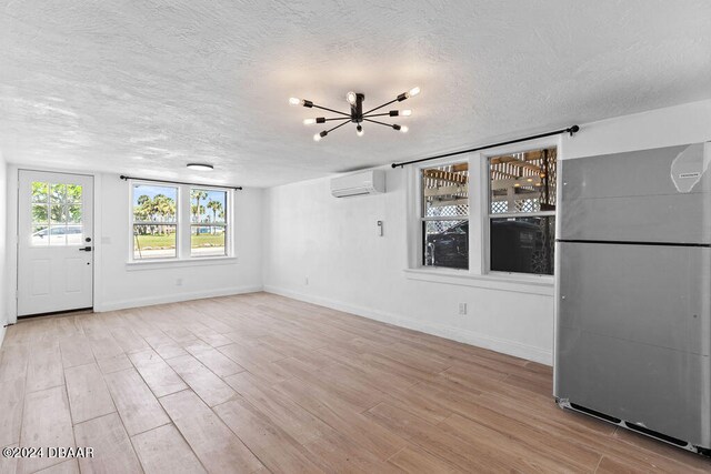 unfurnished living room with a wall unit AC, light hardwood / wood-style flooring, a textured ceiling, and an inviting chandelier