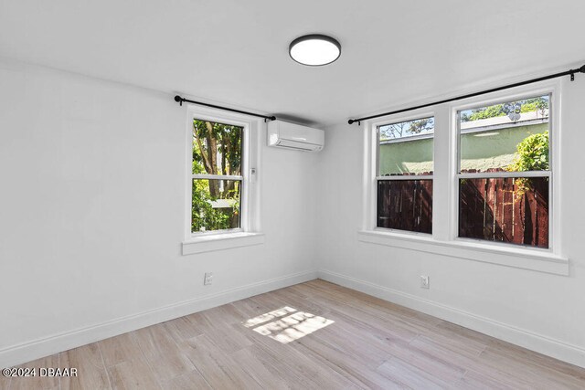 empty room featuring light hardwood / wood-style floors, a wealth of natural light, and a wall mounted AC