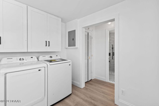 clothes washing area with light wood-type flooring, electric panel, washing machine and clothes dryer, and cabinets