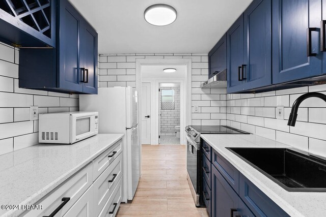 kitchen with light stone counters, blue cabinetry, sink, white appliances, and light hardwood / wood-style flooring