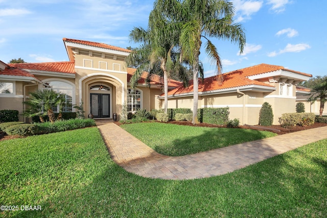 mediterranean / spanish-style house featuring french doors, a front lawn, a tile roof, and stucco siding