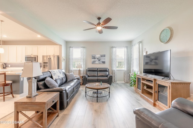 living area with light wood-style flooring, a textured ceiling, and a ceiling fan