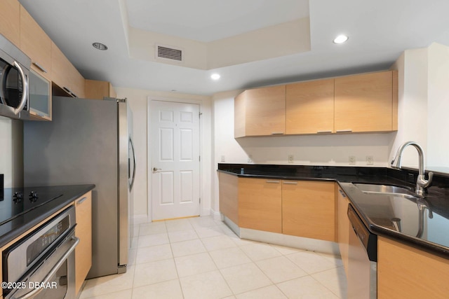 kitchen with visible vents, a tray ceiling, stainless steel appliances, light brown cabinetry, and a sink