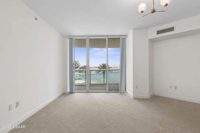 carpeted empty room with floor to ceiling windows, visible vents, baseboards, and an inviting chandelier