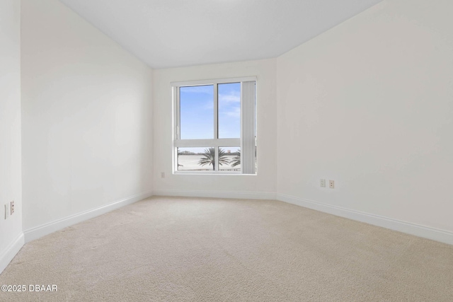 empty room with baseboards, vaulted ceiling, and light colored carpet