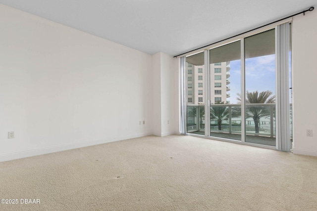 carpeted spare room featuring a wall of windows and baseboards