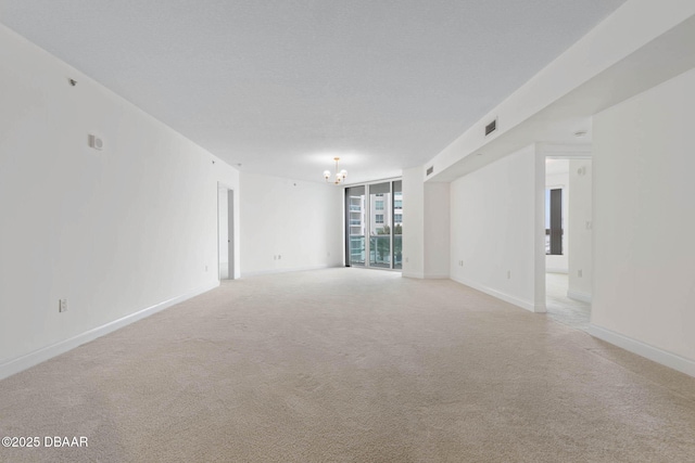 empty room featuring an inviting chandelier, baseboards, visible vents, and light colored carpet