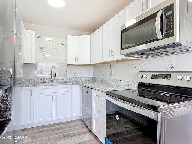 kitchen featuring a sink, light stone counters, appliances with stainless steel finishes, and white cabinets