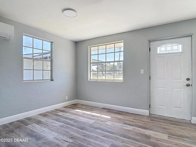 foyer entrance featuring a textured wall, a wall mounted air conditioner, baseboards, and wood finished floors