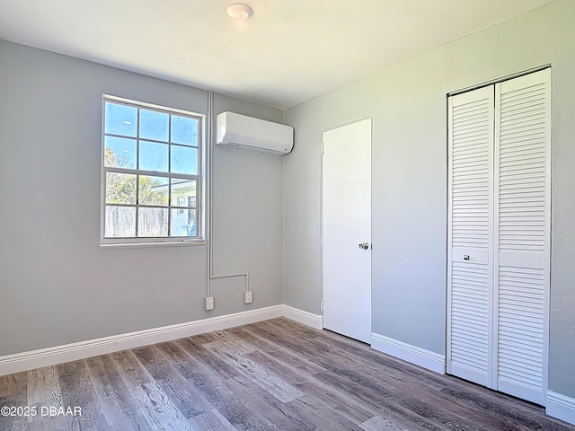 unfurnished bedroom featuring a wall mounted air conditioner, a closet, baseboards, and wood finished floors