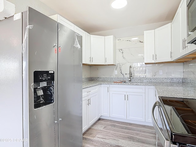 kitchen featuring a sink, light wood-style floors, appliances with stainless steel finishes, white cabinets, and light stone countertops