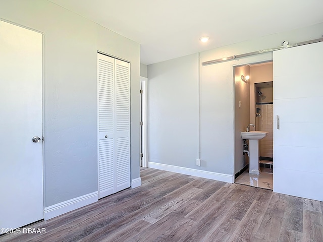 unfurnished bedroom featuring a closet, baseboards, ensuite bath, and wood finished floors