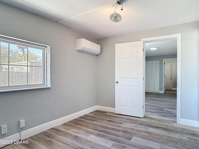 unfurnished room with baseboards, an AC wall unit, and wood finished floors