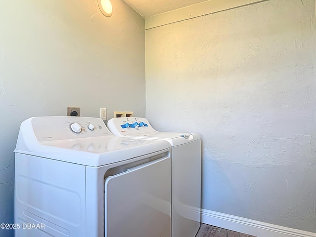 clothes washing area featuring washing machine and clothes dryer, baseboards, wood finished floors, laundry area, and a textured wall