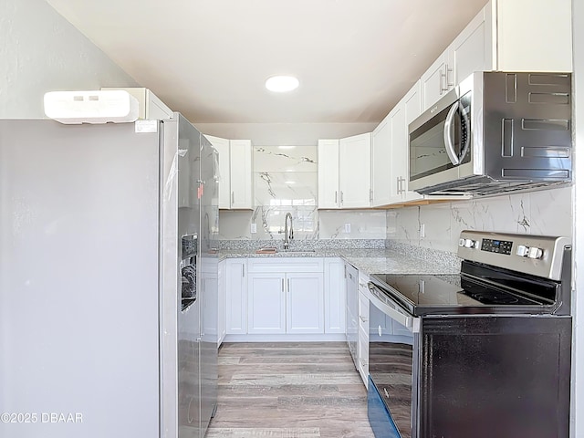 kitchen with light stone countertops, light wood-style floors, white cabinets, stainless steel appliances, and a sink